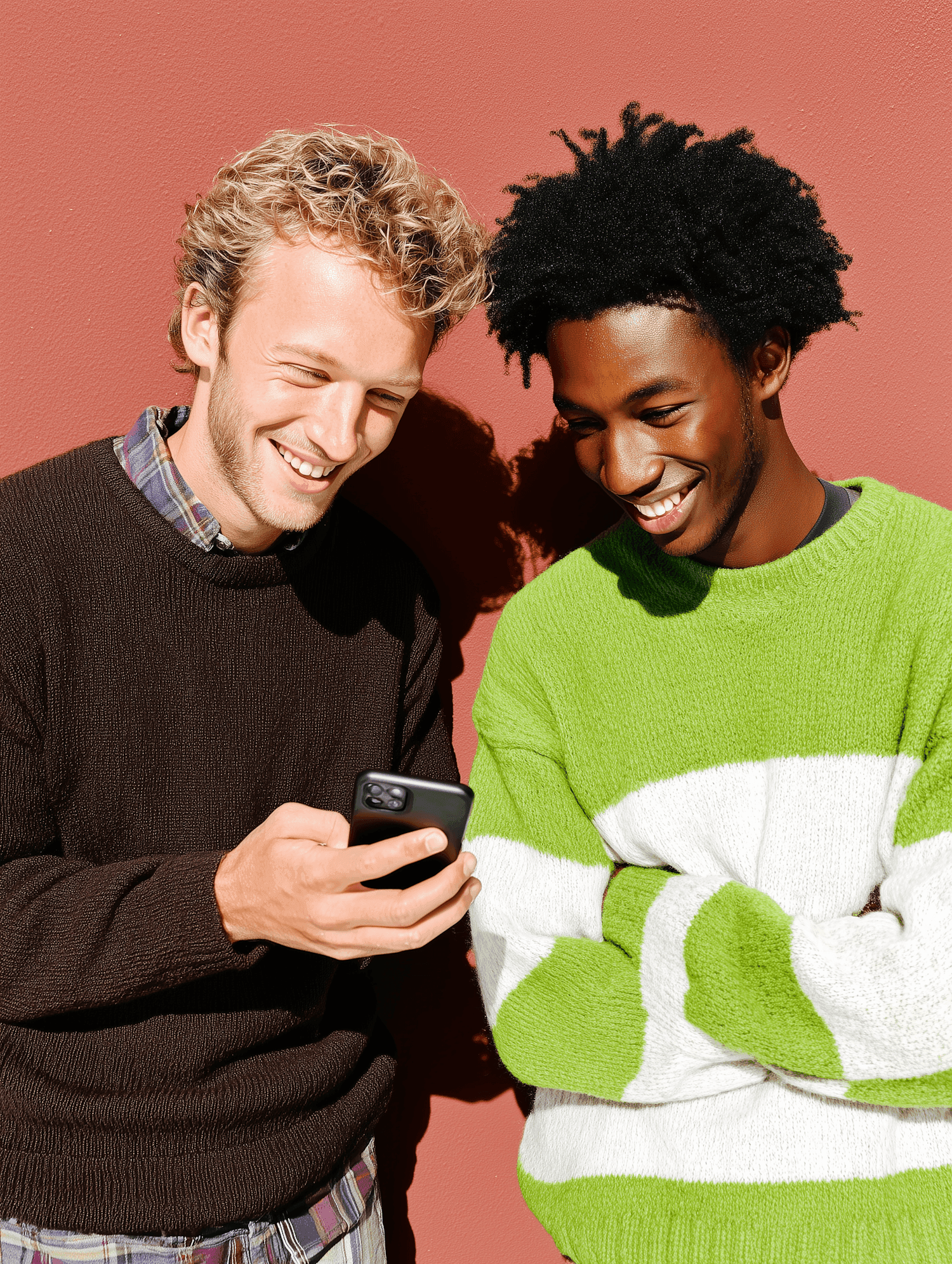 Two friends smiling at a phone in front of a terracotta wall