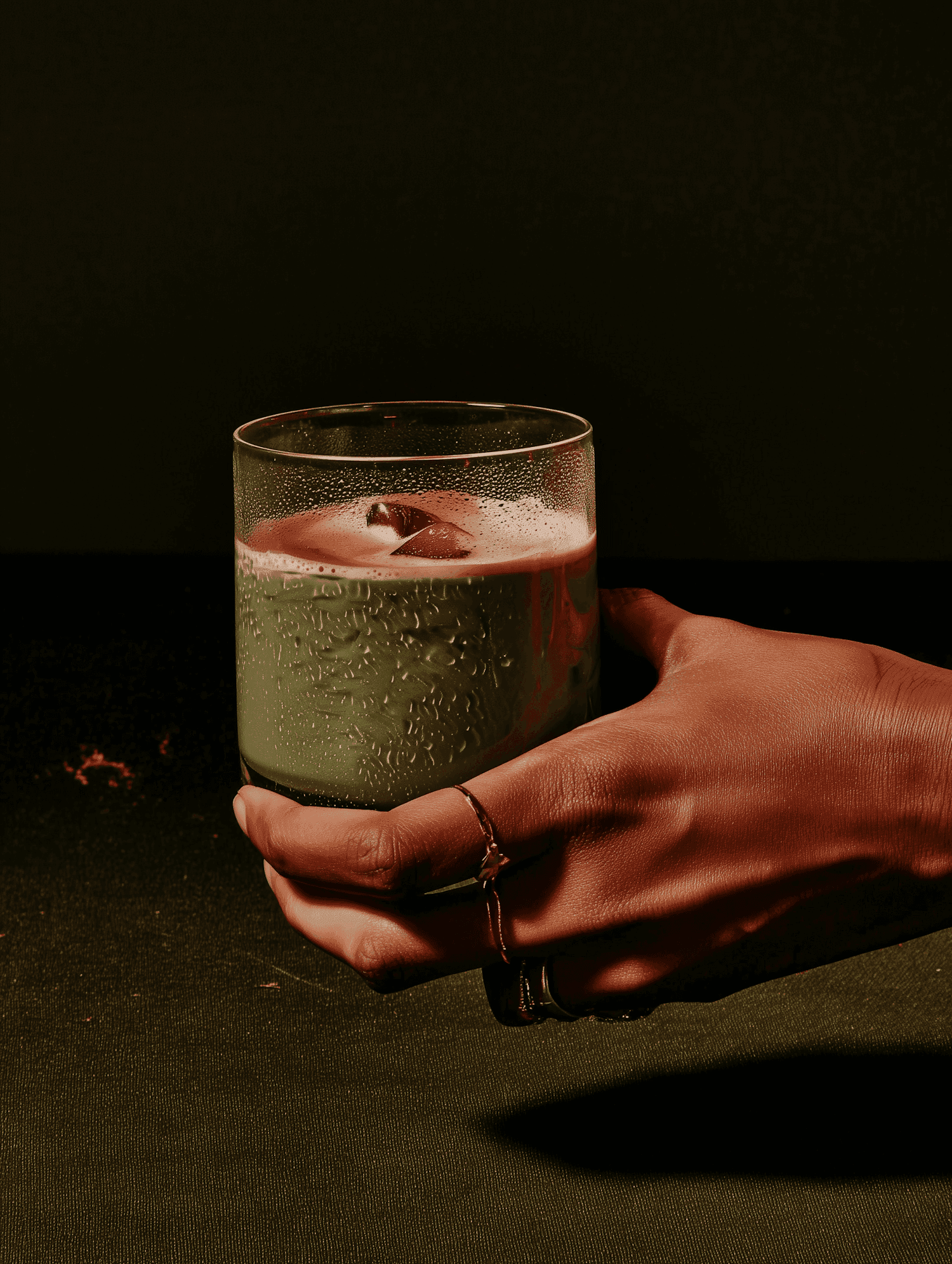 Hand holding a frosted glass of green drink against a dark backdrop