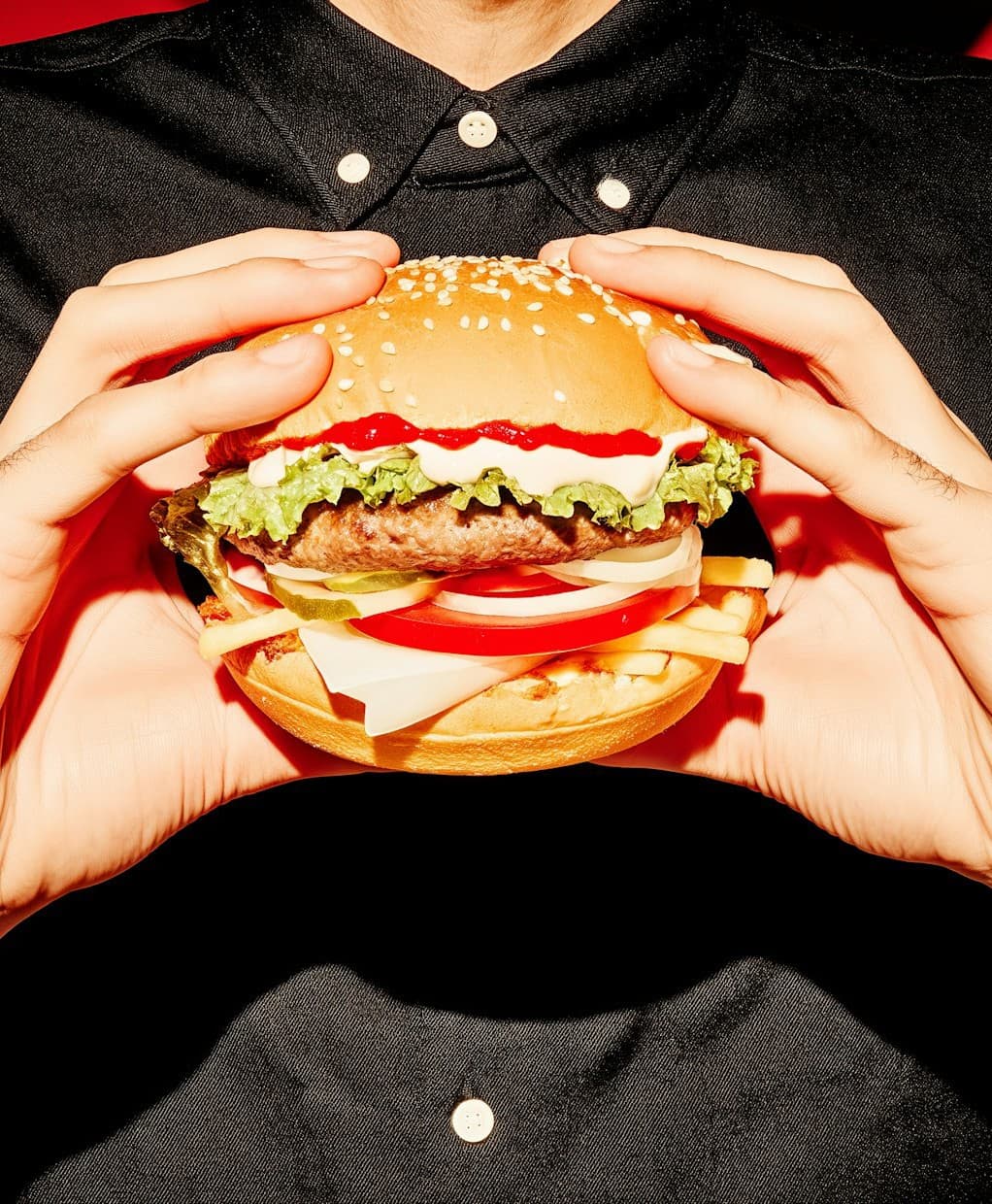 Hands holding a stacked burger against a black shirt